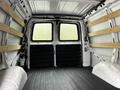 A 2023 GMC Savana cargo van interior with bare walls and wooden shelving installed, featuring a rubber floor and double doors at the back