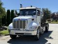 A silver 2019 Peterbilt 337 truck with a flatbed and visible grill and headlights is parked facing forward with orange lights on the roof