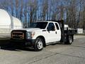 A white 2011 Ford F-350 SD pickup truck with a flatbed and black tool box mounted in the rear