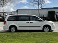 A white 2011 Dodge Grand Caravan parked on grass with a side view showcasing its sleek design and alloy wheels