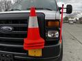 A 2011 Ford Econoline van with a stacked set of three orange traffic cones and a traffic wand mounted on the front grille