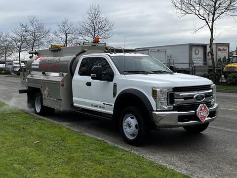 A white 2018 Ford F-550 with a fuel tank on the back and safety markings on the side parked on a road