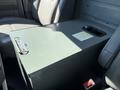 A grey metal storage box with a lid and cup holders is positioned between two front seats in a 2011 Ford Econoline