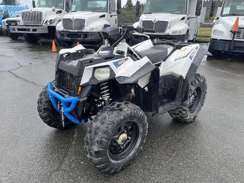 A 2017 Polaris Scrambler all-terrain vehicle with a black and white body and large rugged tires parked on a wet surface