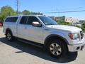 A silver 2014 Ford F-150 with an extended cab and a matching camper shell on the bed features large alloy wheels and black step bars