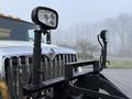 A 2016 International 7400 truck with a silver front grille and mounted lights on a plow frame in the foreground