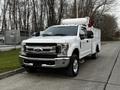 A white 2019 Ford F-350 SD with a service body and equipment mounted on the roof parked on a street