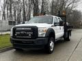 A 2015 Ford F-550 truck with a white exterior and a black flatbed with safety rails in the rear