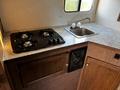 A modern kitchen interior featuring a two-burner gas stove and a stainless steel sink with a faucet on a counter with a light-colored surface and wooden cabinets