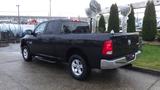 A black 2017 RAM 1500 pickup truck is parked with its bed covered and its tailgate open displaying the rear lights and logo