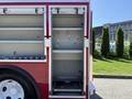 An empty compartment of a red and white 1991 International 4600 fire truck with shelves and hooks for storing equipment