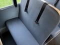 A gray bus seat with a smooth surface and two black seat belts attached to the back is visible in the foreground