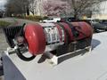 A red fire extinguisher mounted on a white metal base with a hose attached on top and a instructions label visible