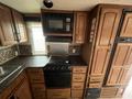 A 2013 Outdoor Wind River kitchen featuring wooden cabinetry a microwave an oven a sink and a countertop with a patterned backsplash