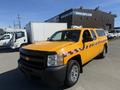 A 2013 Chevrolet Silverado 1500 in bright yellow with a checkered pattern on the sides parked with a cap on the truck bed