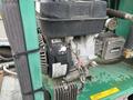 A close-up view of a Hightliner Aquacide Hot Water Weed Control engine with visible wiring components and a gauge attached on a green flat deck trailer