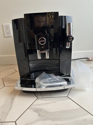 A Jura E8 Fully Automatic Espresso Machine in black with a chrome coffee dispenser and a water container placed next to it