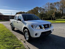 A 2015 Nissan Frontier pickup truck in white with chrome accents and a crew cab design parked on a roadway