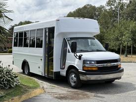 A white 2017 Chevrolet Express shuttle bus with a high roof and large windows parked with its door open
