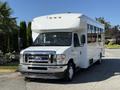 A white 2021 Ford Econoline bus with a large windshield and multiple windows on the side parked in a paved area