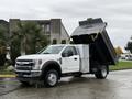 A white 2021 Ford F-550 dump truck with the bed raised in a dumping position