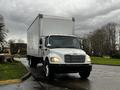 A white 2018 Freightliner M2 106 box truck with a large cargo area and front headlights illuminated