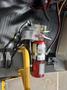 A red fire extinguisher is mounted on the floor of a vehicle with safety instructions visible next to it