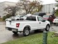A white 2018 Ford F-150 pickup truck parked on a wet surface with its bed empty and chrome accents on the rear taillights and bumpers