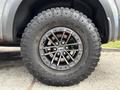 A close-up of a large rugged tire mounted on a black alloy wheel featuring five spokes and a chrome center cap with the Ford logo