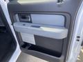 Interior door panel of a 2012 Ford F-150 featuring a gray armrest and handle with a textured black bottom section and a small storage area