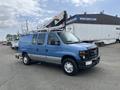 A blue 2010 Ford Econoline van equipped with a ladder rack is parked with its side facing the viewer
