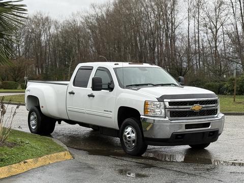 A 2013 Chevrolet Silverado 3500HD pickup truck with a white exterior and chrome accents parked at an angle with its headlights on