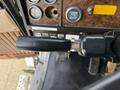 A close-up of the gear shift lever in a 1996 Kenworth T800 truck with various dashboard gauges and controls visible in the background