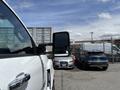 A white 2020 Chevrolet Silverado with a prominent side mirror is parked in a lot with other vehicles visible in the background