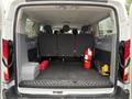 The interior of a 2017 Ford Transit T150 XLT with empty cargo space featuring gray bench seats and storage containers including a red toolbox and a fire extinguisher
