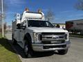 A 2018 Ford F-550 with a white body and an elevated platform on the back, equipped with amber lights on top and a large front grille