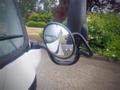 A 2003 Toyota Toyoace with a side mirror reflecting the road and a blurred view of greenery in the background