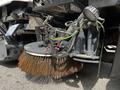 Close-up of a 2012 Autocar Xpert street cleaning machine with a large rotating broom attached featuring metal bristles and various connected wires and controls