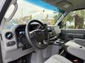 Interior view of a 2022 Ford E-450 with a steering wheel dashboard controls and a center console featuring cup holders and soft gray upholstery