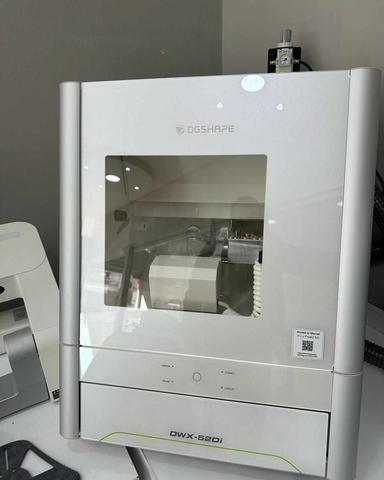 A Roland DWX-52D 5-Axis Dental Milling Machine with a transparent front panel displaying its internal components and a control panel at the bottom