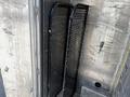 A black metal mesh rack leaning against a wall with a hook next to it inside a vehicle compartment