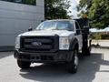 A 2016 Ford F-550 truck with a gray exterior and orange lights on the roof parked in a lot with a black utility bed and large wheels