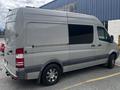 A silver 2010 Mercedes-Benz Sprinter van with a high roof and sliding side door parked at an angle with blacked-out windows and alloy wheels
