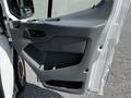 A 2015 Ford Transit van's driver side door panel featuring controls and a handle with textured finishes and storage compartments