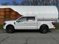 A 2021 Ford F-150 pickup truck in white with a crew cab and black rims parked on the street