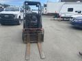 A 2010 Toyota 7FGGU25 forklift viewed from the front with two long metal forks extended forward and an operator's seat visible behind the forks