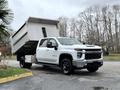 A white 2021 Chevrolet Silverado 3500HD pickup truck with a dump bed is shown tilted at an angle conveying a loading position