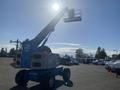A blue 1997 Genie S-65 4X4 aerial lift with a raised arm and platform for workers is positioned prominently in the image