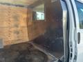 Interior view of a 2012 Chevrolet Express van showing a metal partition and wooden wall with a window cutout for visibility