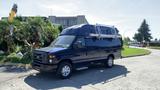 A blue 2013 Ford Econoline van with a roof rack and large tires parked on a concrete surface